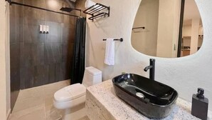 Une salle de bain moderne avec une douche aux couleurs sombres, des toilettes blanches et un grand miroir ovale.