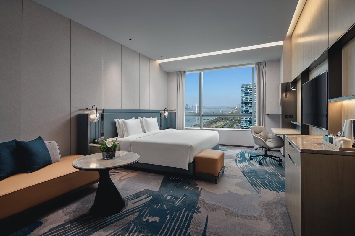 Quarto de hotel moderno com uma cama grande, um sofá, uma escrivaninha e uma televisão.