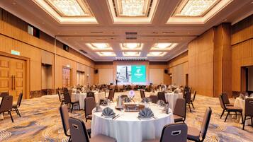 A large conference room with round tables, chairs, and a large screen at the front.
