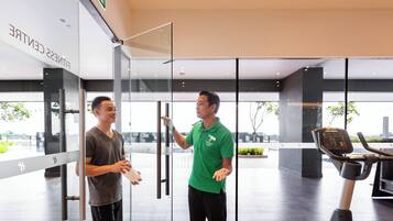 Dos personas en un gimnasio moderno con puertas de vidrio, una cinta de correr y vistas al exterior.