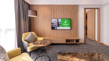 Habitación de hotel con zona de estar, televisor montado en la pared y diseño de paneles de madera.