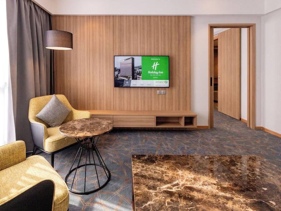 Habitación de hotel con zona de estar, televisor montado en la pared y diseño de paneles de madera.