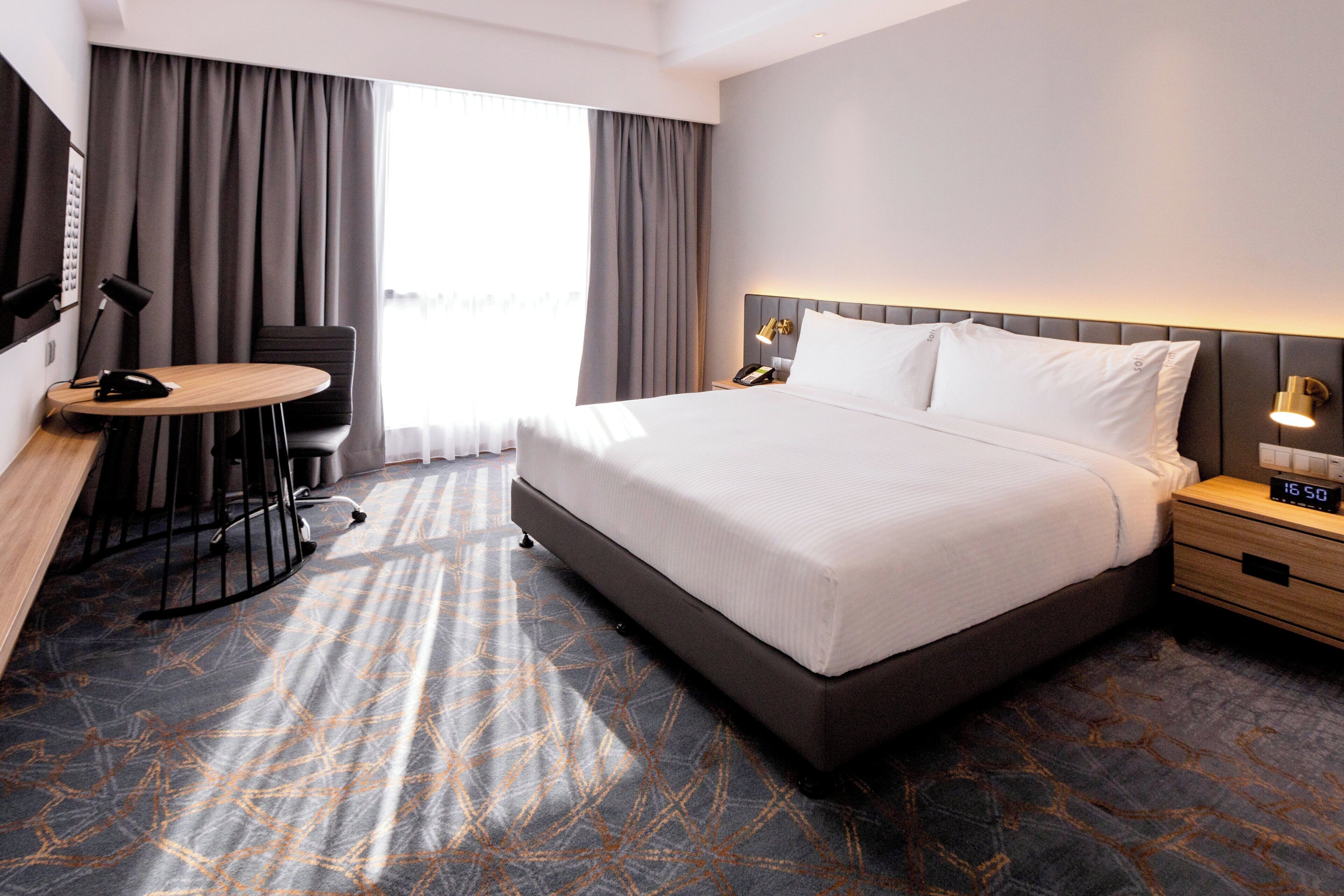 Hotelkamer met een groot bed, een bureau met stoel, nachtkastje met lamp en uitzicht op het omliggende landschap door het raam.
