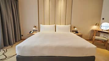 Quarto de hotel com uma cama grande, mesas de cabeceira com luminárias, uma escrivaninha com cadeira e uma janela ampla com cortinas.