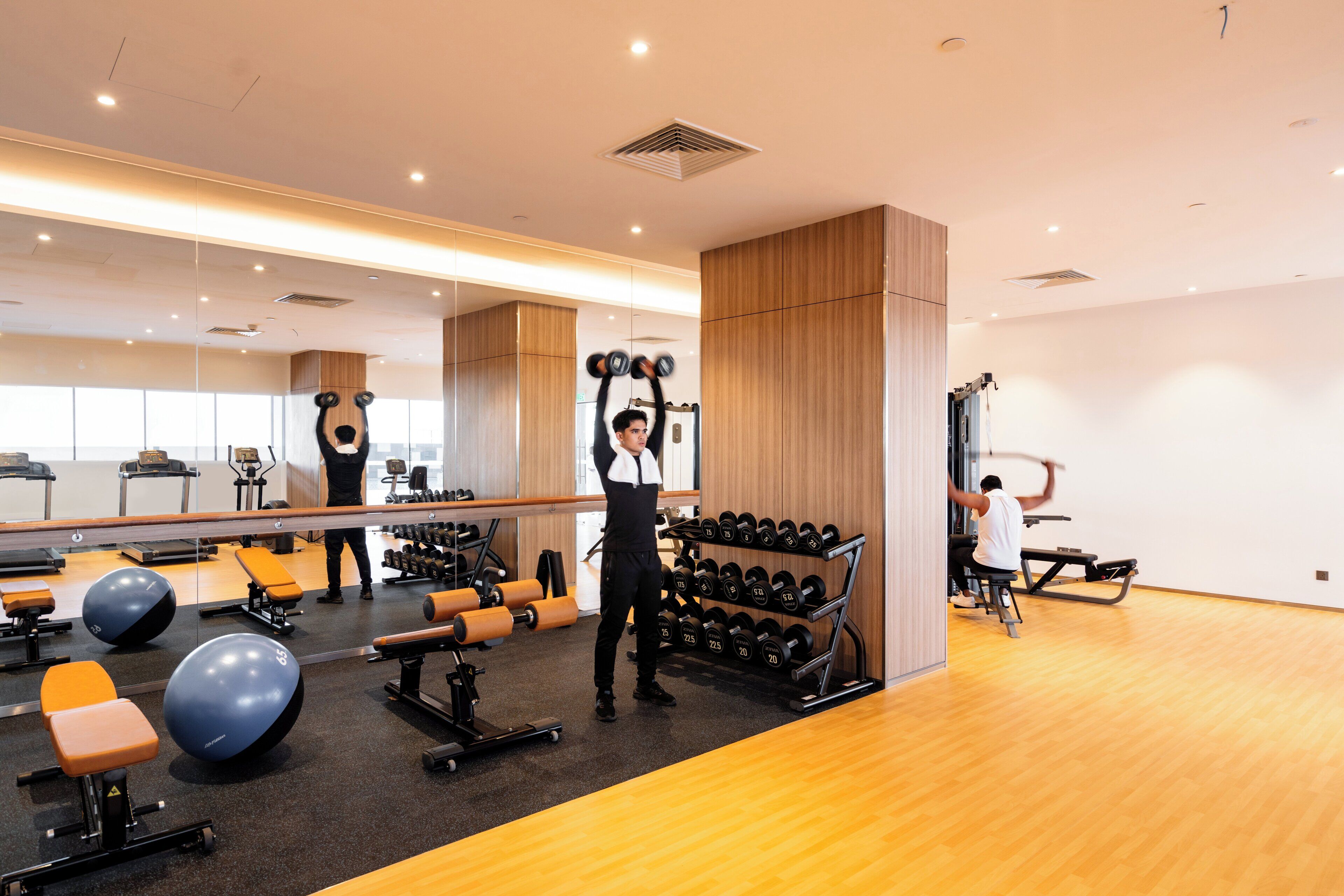 A gym with exercise equipment, a mirror, and wooden flooring.