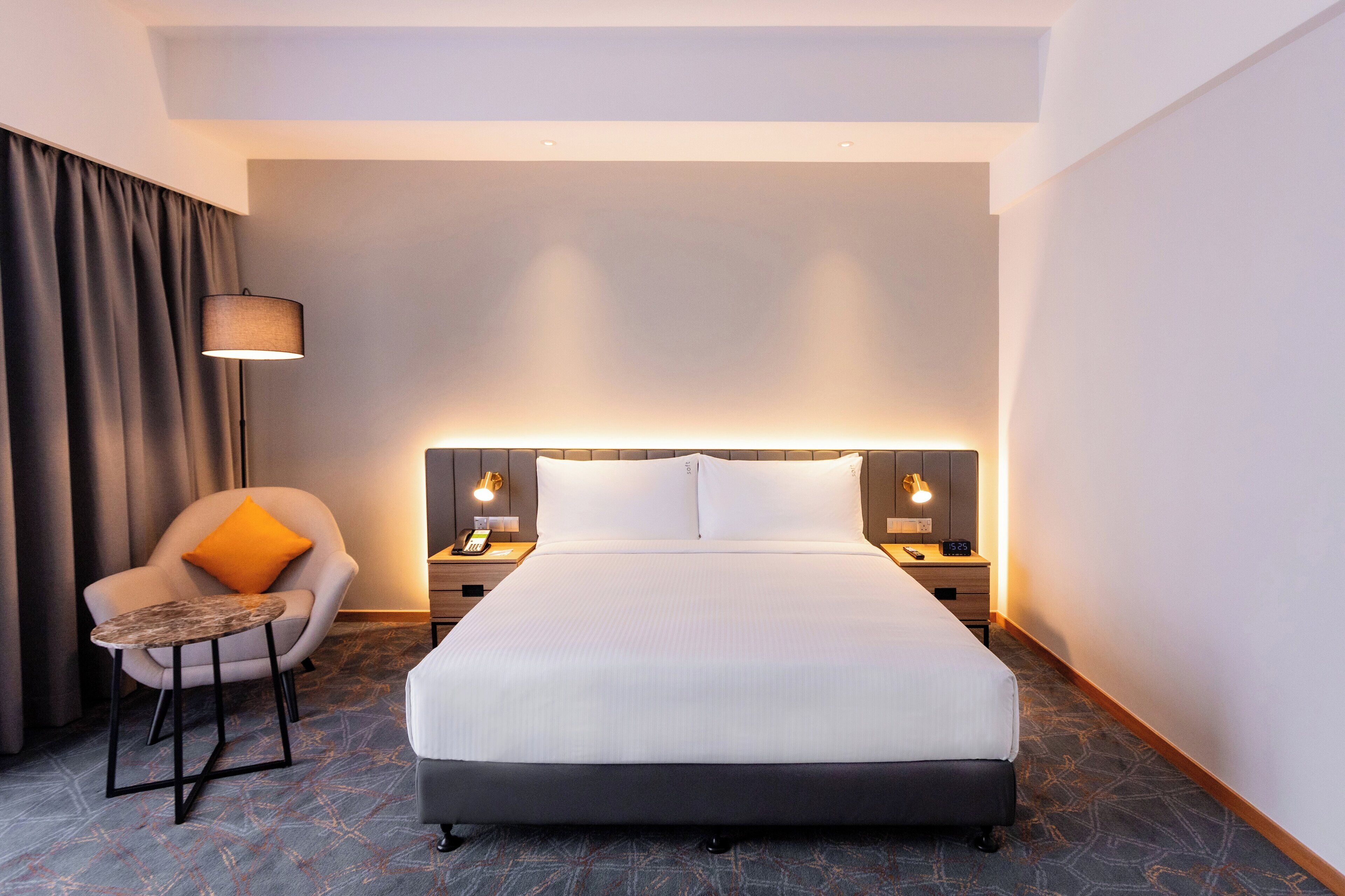 A hotel room with a large bed, a chair with a small table, two bedside tables with lamps, and a curtain.