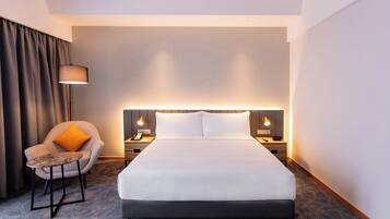 A hotel room with a large bed, a chair with a small table, two bedside tables with lamps, and a curtain.