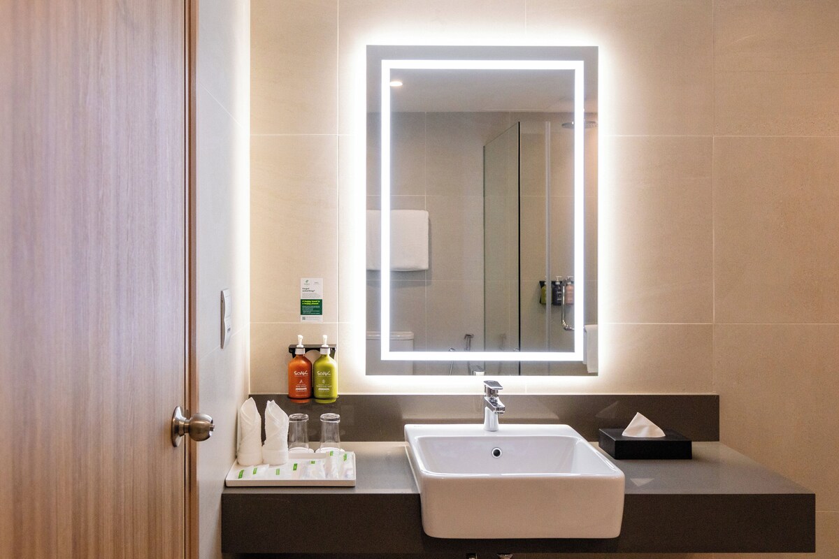 A modern bathroom with a large mirror, a sink, and toiletries on the counter.