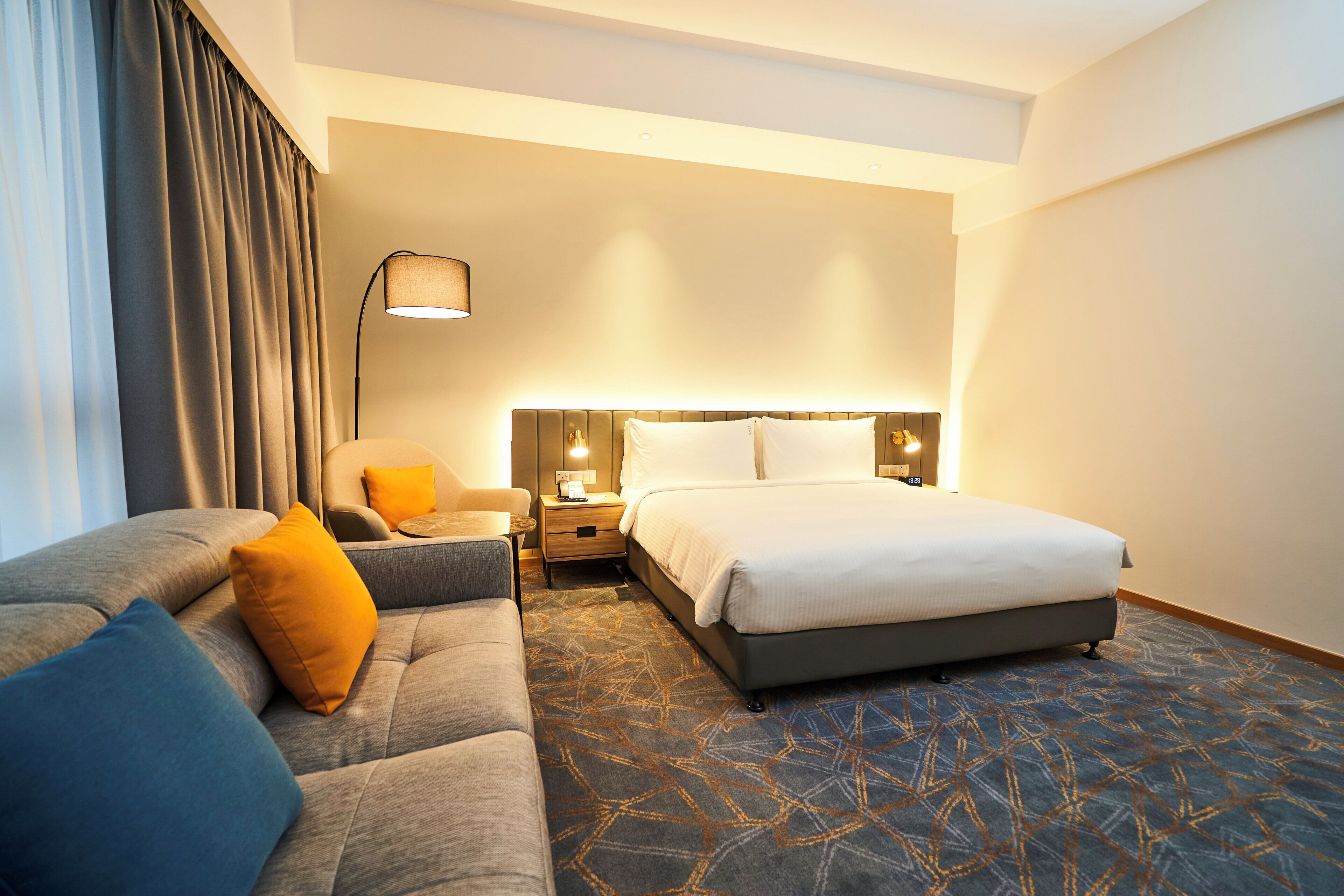 A hotel room with a bed, a sofa, a nightstand, a lamp, and a window with curtains.