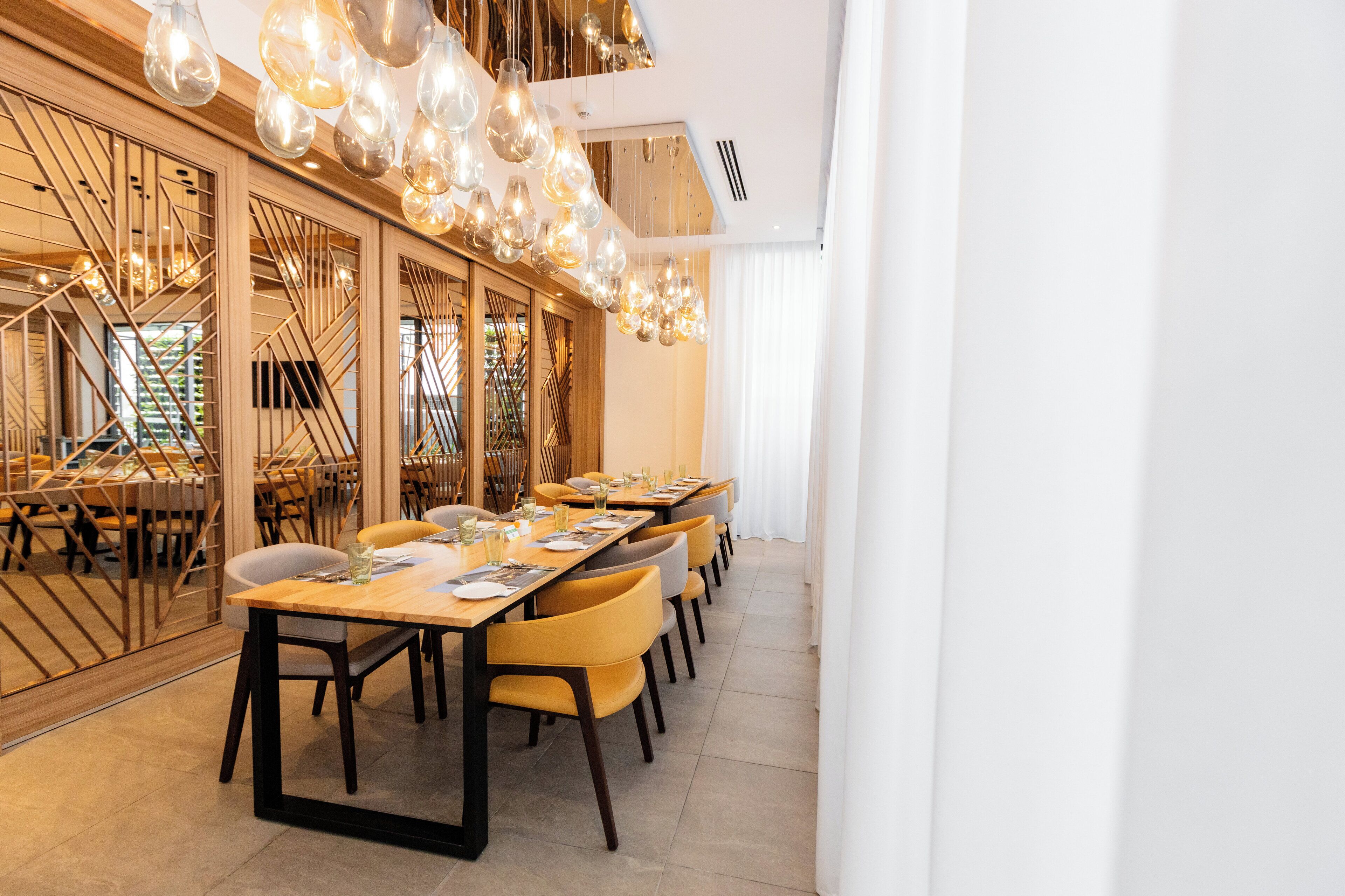 A modern dining area with long tables, yellow chairs, and a unique geometric glass partition.
