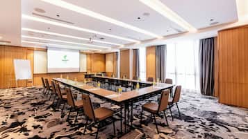 Un salón de conferencias con una larga mesa, sillas, una pantalla de proyector y una pizarra.