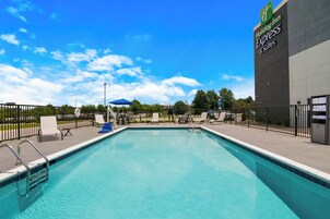 Un Holiday Inn Express & Suites con una piscina azul cristalina, sillas de descanso y un área de patio cercada.