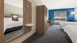 Quarto de hotel com um espelho grande, um guarda-roupa de madeira, uma escrivaninha com cadeira e duas camas.