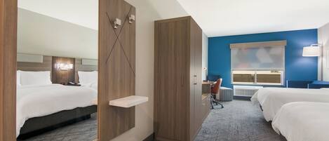 Une chambre d’hôtel avec un grand miroir, une armoire en bois, un bureau avec une chaise et deux lits.