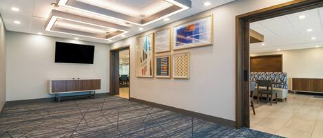 A spacious room with a patterned carpet, a flat-screen TV mounted on the wall, and a wooden bench along one side.