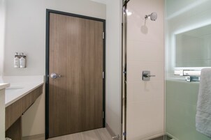 Un baño moderno con puerta de madera, cabina de ducha de vidrio y lavamanos blanco.