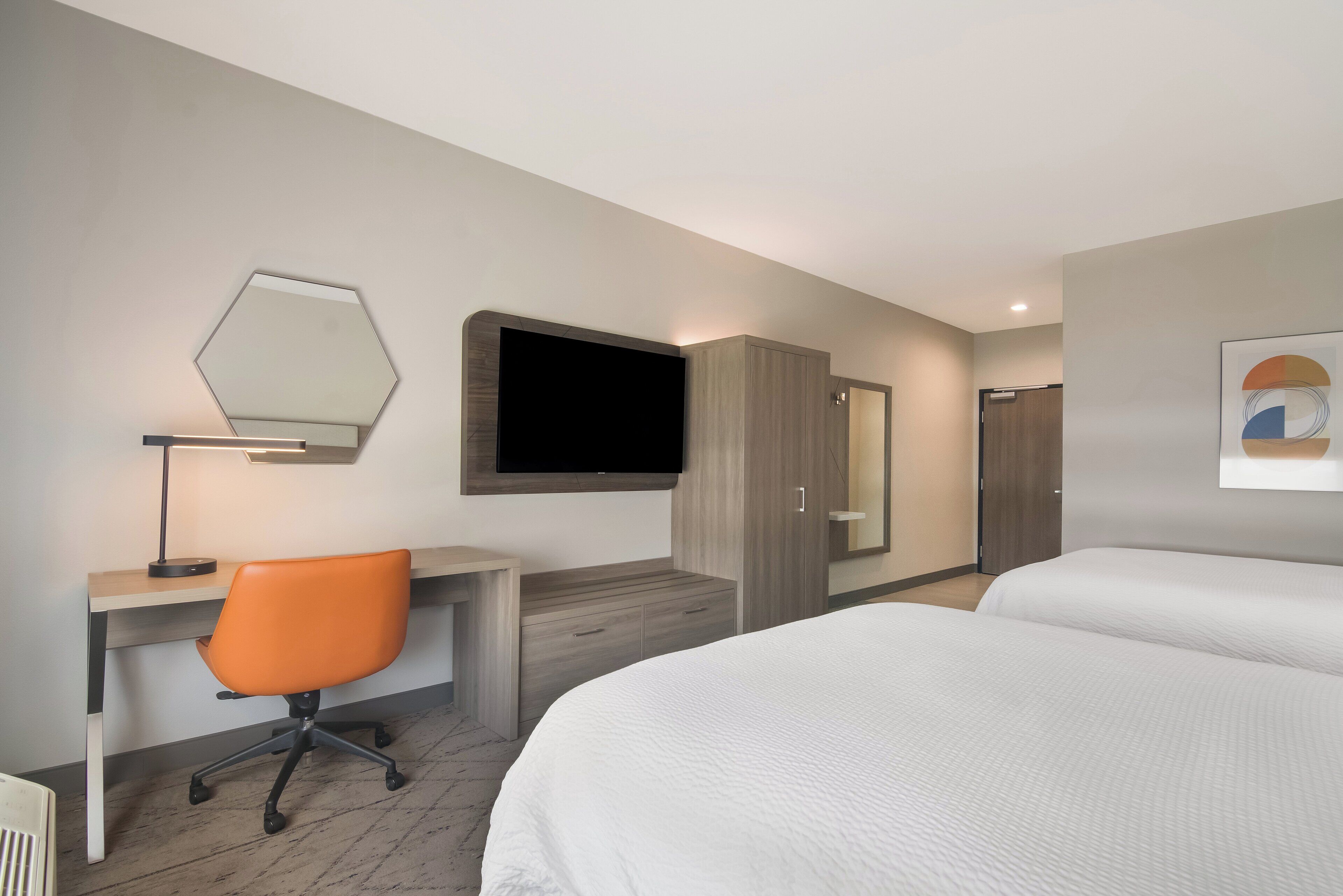 A hotel room with a bed, a desk with a chair, a TV, and a wardrobe.