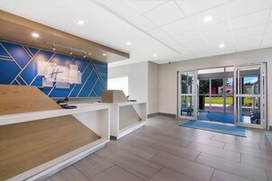 Un área de recepción con diseño moderno, que incluye un mostrador de madera, una pared azul con motivos geométricos y una puerta de cristal que da al exterior.