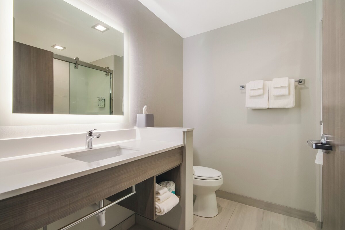 A modern bathroom with a large mirror, a sink, a toilet, and a shower area.