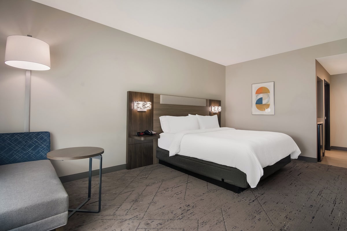 Una habitación de hotel con una cama, mesita de noche, lámpara y una silla azul.