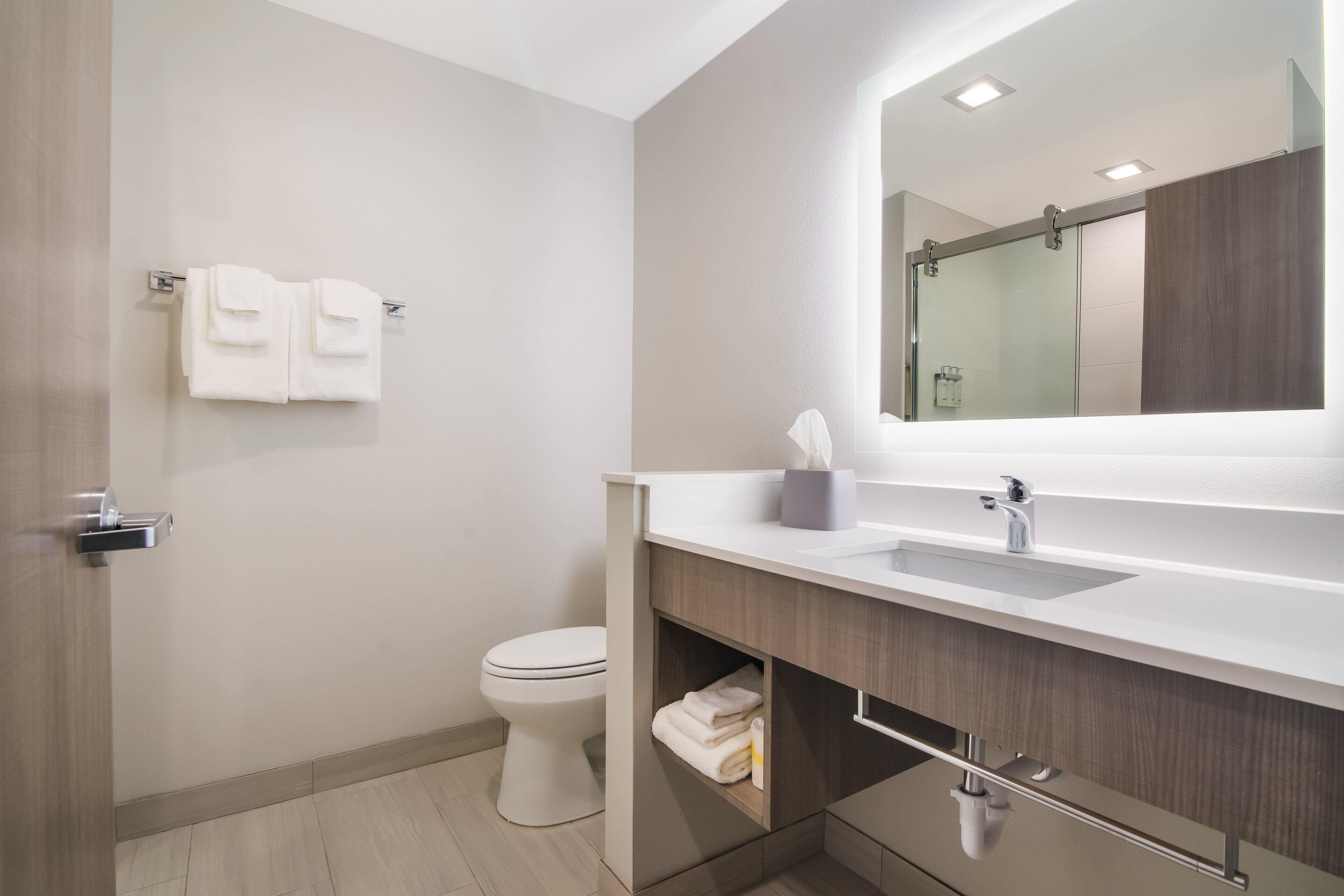 A modern bathroom with a white toilet, a large mirror, and a vanity with a sink.