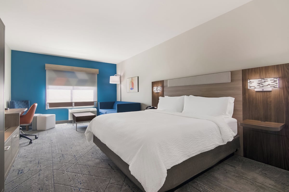 Una habitación de hotel moderna con una cama grande, un escritorio con una silla, una pared de acento azul y una ventana.