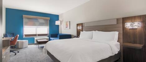 A modern hotel room with a large bed, a desk, a chair, and a window.