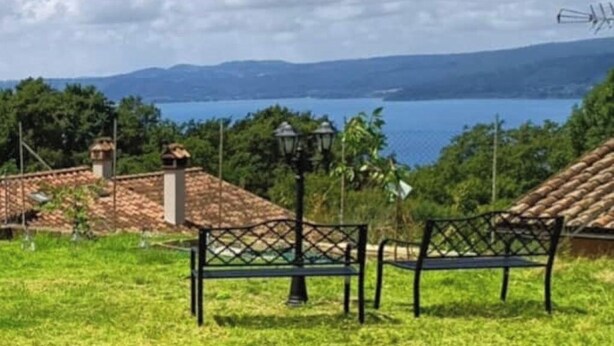 A grassy area with a bench and a lamp post, overlooking a body of water and distant mountains. - La Rosa - Romantic lake view apartment (Trevignano Romano)