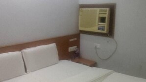 A hotel room with a bed, a nightstand, a wall-mounted air conditioning unit, and a power outlet. - Hotel Celebration (Deoria)