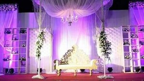 A stage with a white sofa, floral arrangements, and a chandelier. - Hotel Celebration (Deoria)