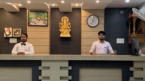 A reception desk with two staff members, a clock, and a decorative statue. - Hotel Celebration (Deoria)