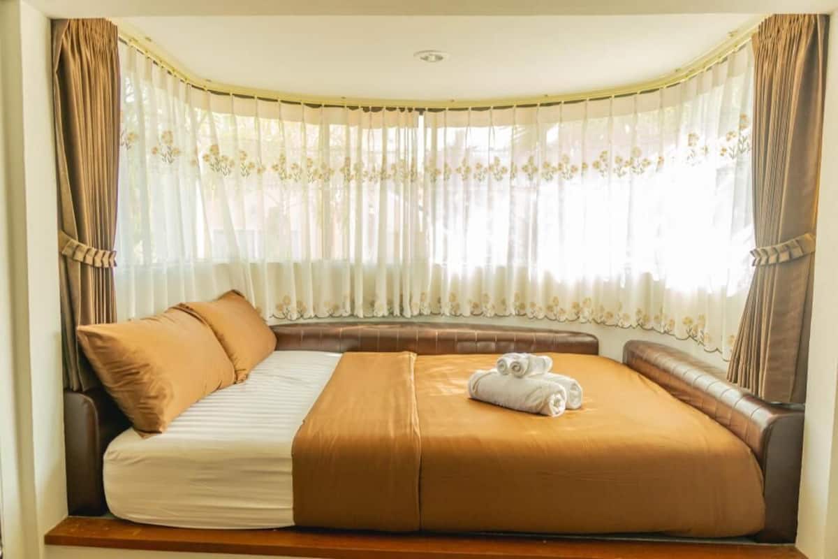 Una habitación de hotel con una cama curvada, un banco y una ventana con cortinas traslúcidas.
