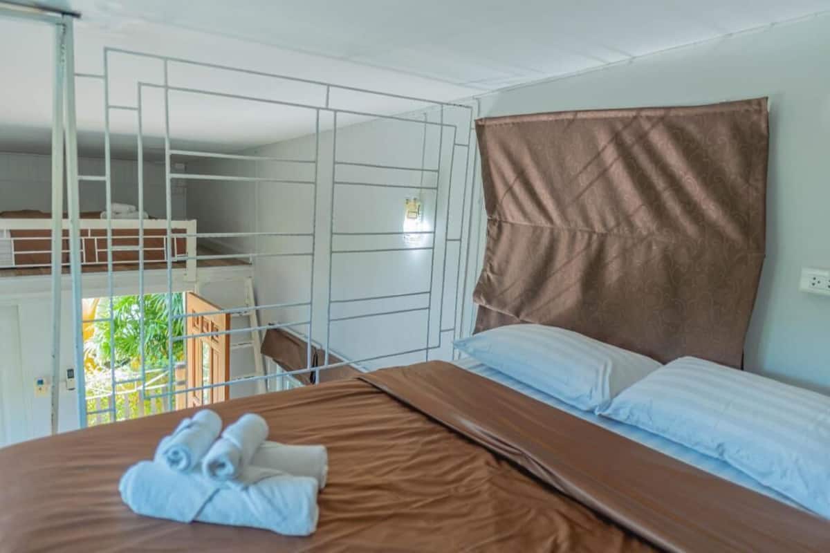 Una cama individual con cabecera marrón, almohadas blancas y una toalla doblada prolijamente a un lado.
