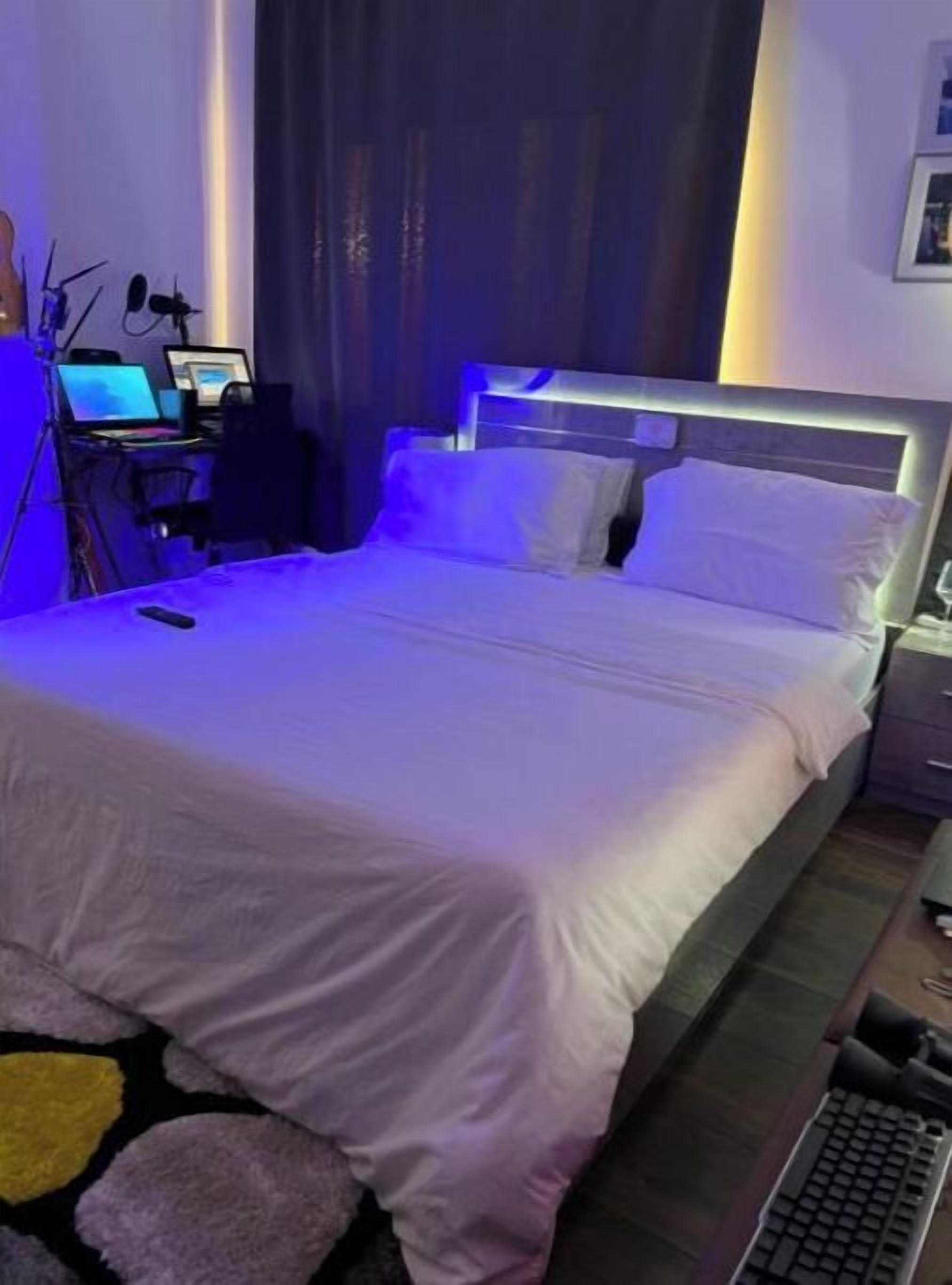 A neatly made bed with a white duvet, a laptop on a desk, and a keyboard on the floor.
