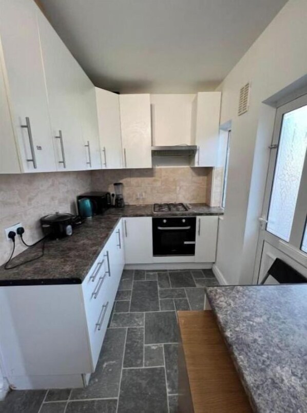 Compact kitchen with oven, stovetop, and range hood.