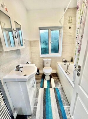 Bathroom features a sink, toilet, and bathtub, with a window for natural light and a striped rug.