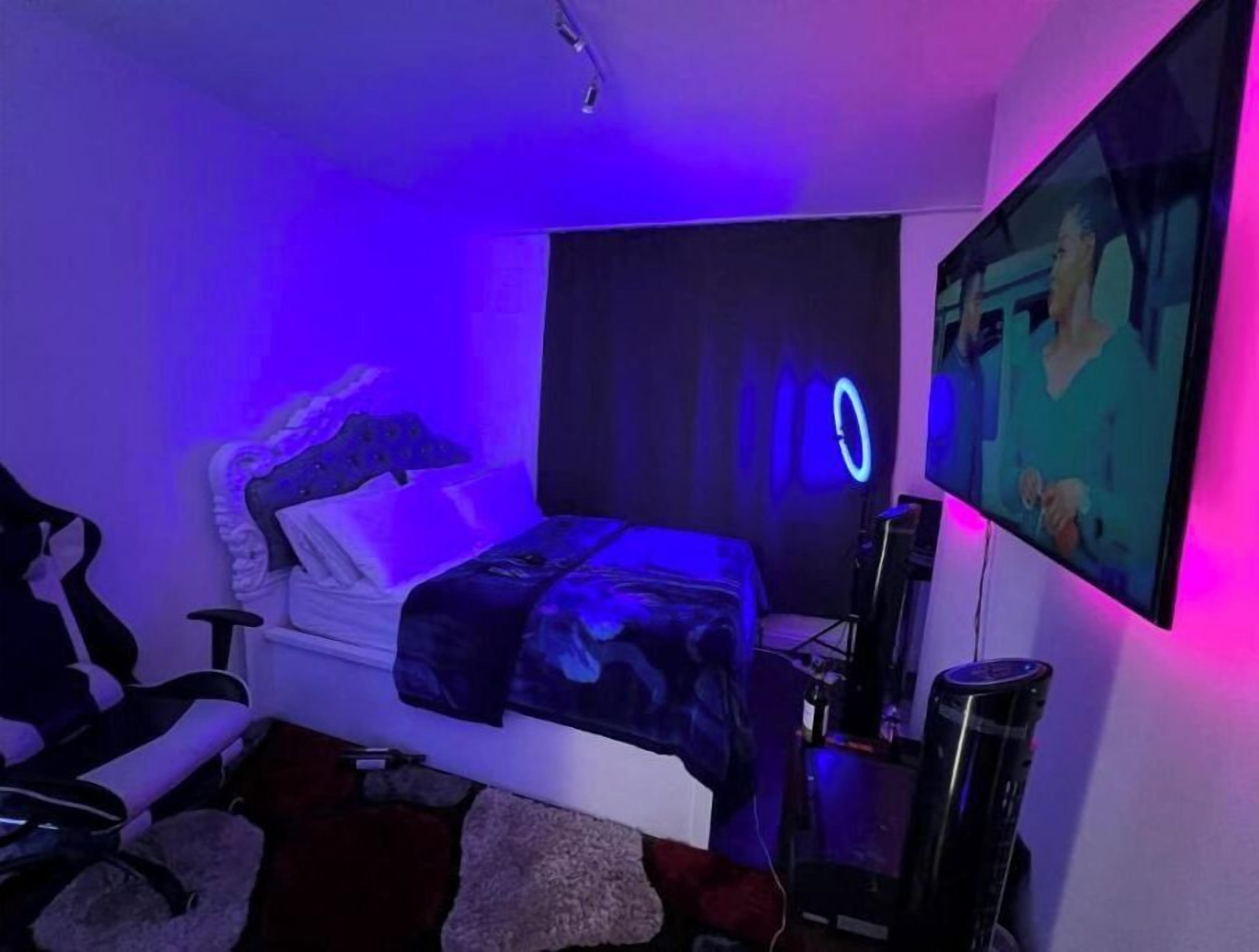 Een slaapkamer met een bed, een aan de muur bevestigde televisie en een gaming-stoel.