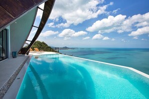 A infinity pool with a clear view of the ocean and a mountainous landscape.