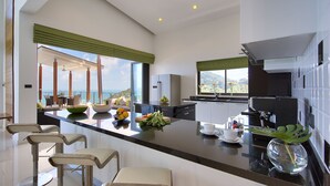 A modern kitchen with a large island, bar stools, and a view of the ocean. - Chaweng Peak Villas - 8 Bedrooms Villa With Infinity Pools (Ko Samui)