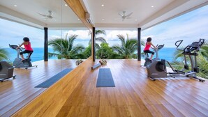 A spacious gym with wooden flooring, exercise equipment, and large windows offering ocean views. - Chaweng Peak Villas - 8 Bedrooms Villa With Infinity Pools (Ko Samui)
