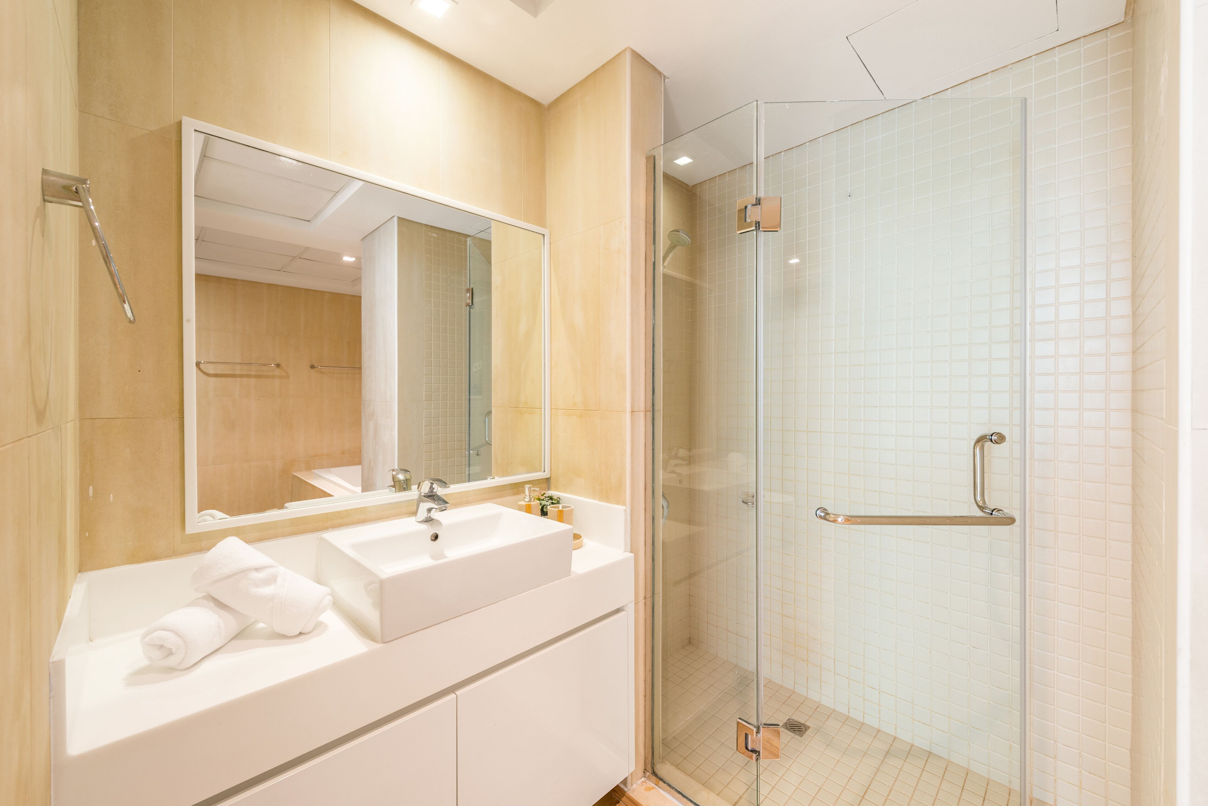 Une salle de bain moderne avec un grand miroir, un lavabo et une douche séparée par une paroi en verre.