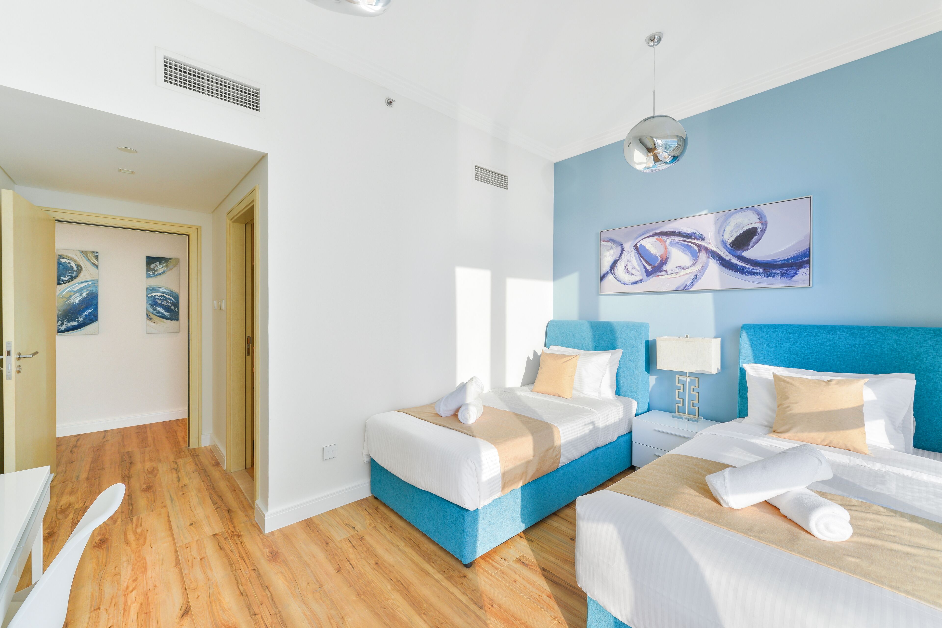 A hotel room with two beds, a blue accent wall, and artwork.