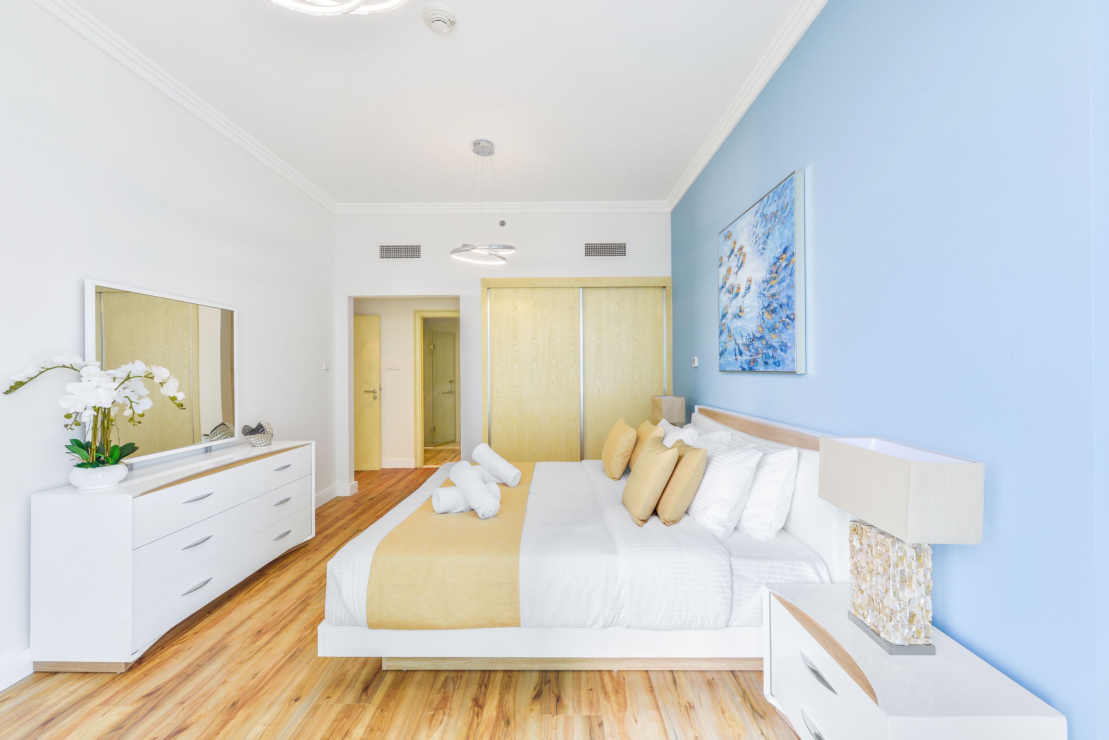 A modern bedroom with a large bed, a white dresser, a mirror, and a blue accent wall.