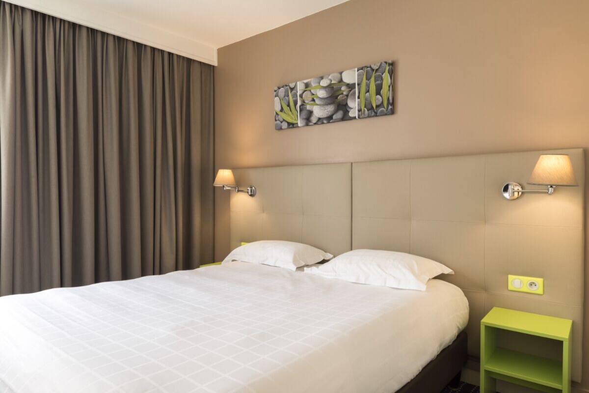 A neatly made bed with white linens, a headboard, and two wall-mounted lamps.