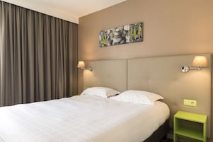 Cama bem arrumada com lençóis brancos, cabeceira e duas luminárias fixadas na parede.