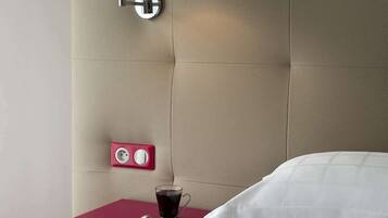Quarto com uma cama, uma mesa de cabeceira com uma xícara de café, uma tomada e um aplique na parede.