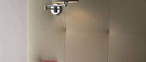 Un dormitorio con cama, una mesita de noche con una taza de café, un enchufe y una lámpara fijada a la pared.