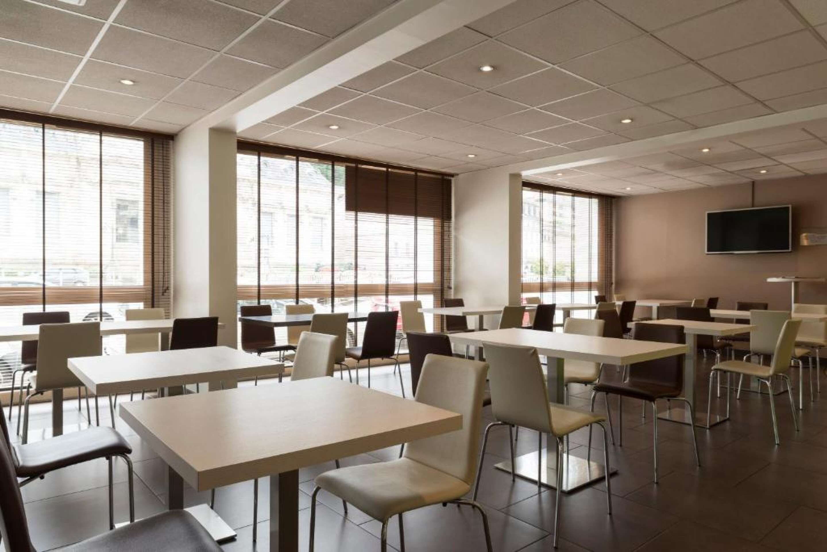 A modern dining area with tables and chairs, large windows, and a flat-screen TV mounted on the wall.