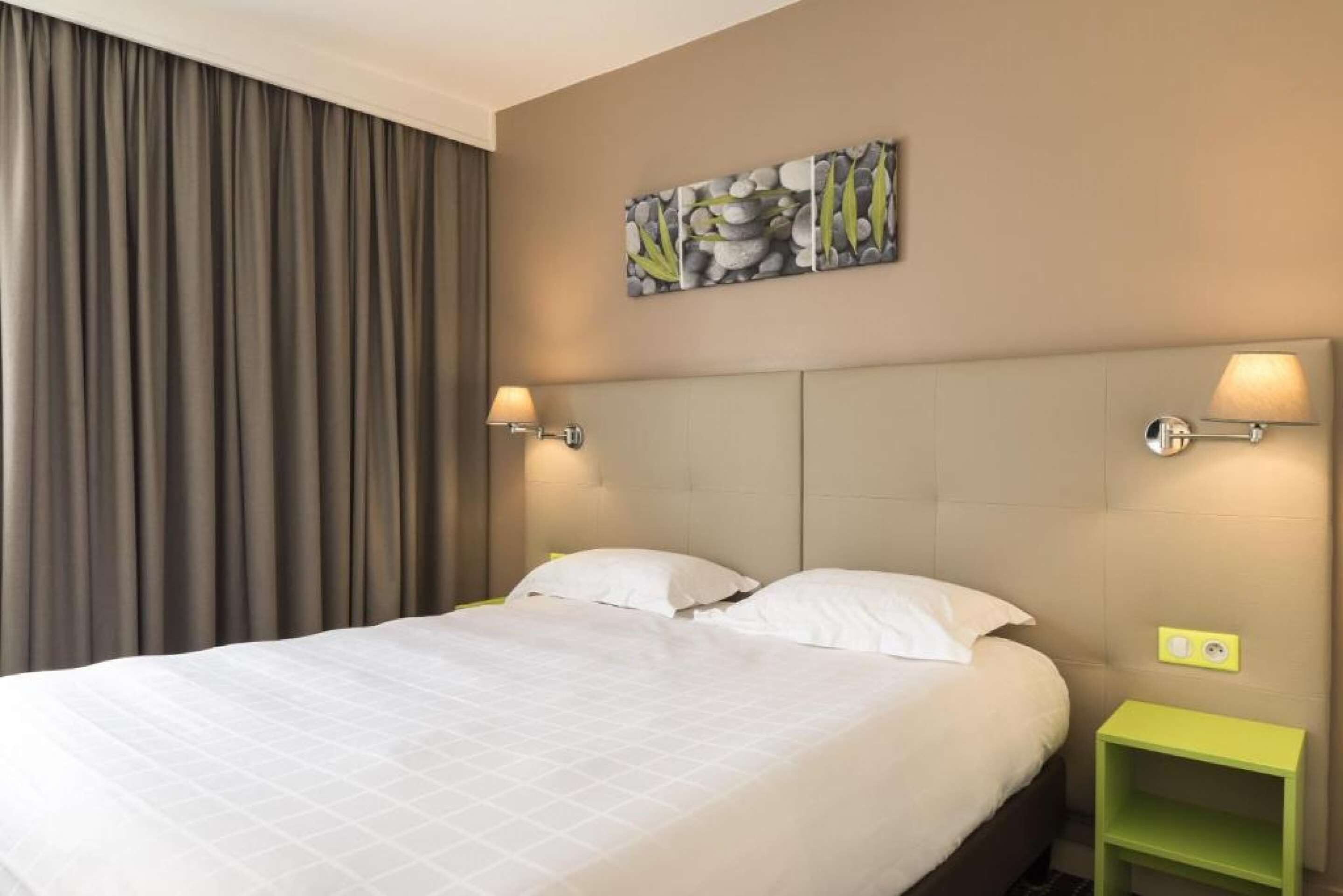 Una habitación de hotel con una cama, dos lámparas de noche, una mesita de noche verde y un cuadro en la pared.