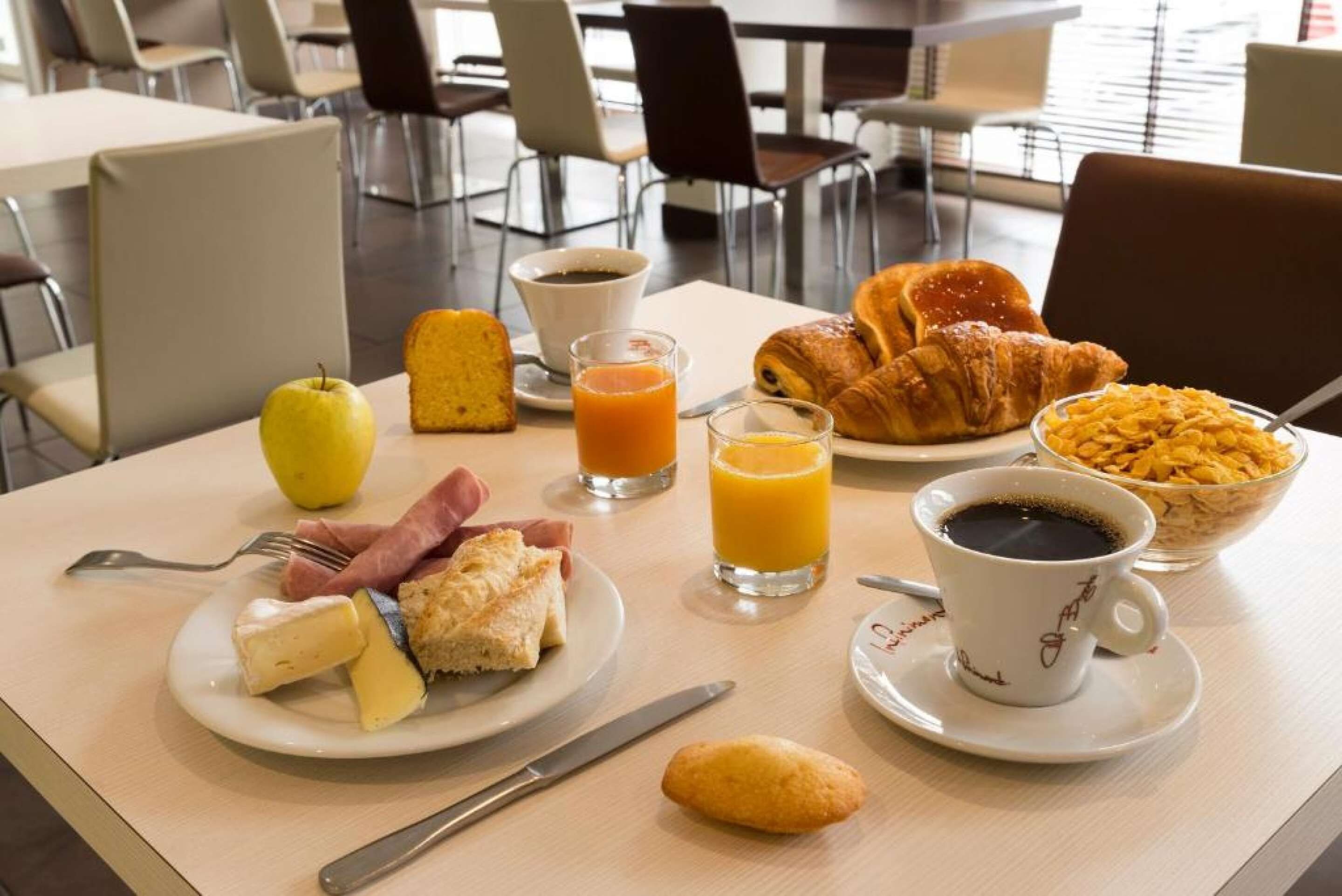 Un desayuno con un plato de comida, un vaso de jugo de naranja, un croissant, un tazón de cereal y una taza de café.